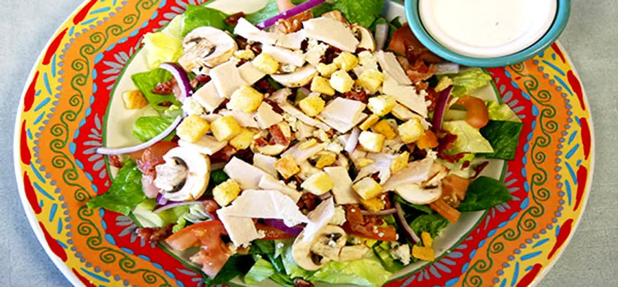 A garden salad piled with turkey, mushrooms, croutons and bacon on a colorful talavera plate